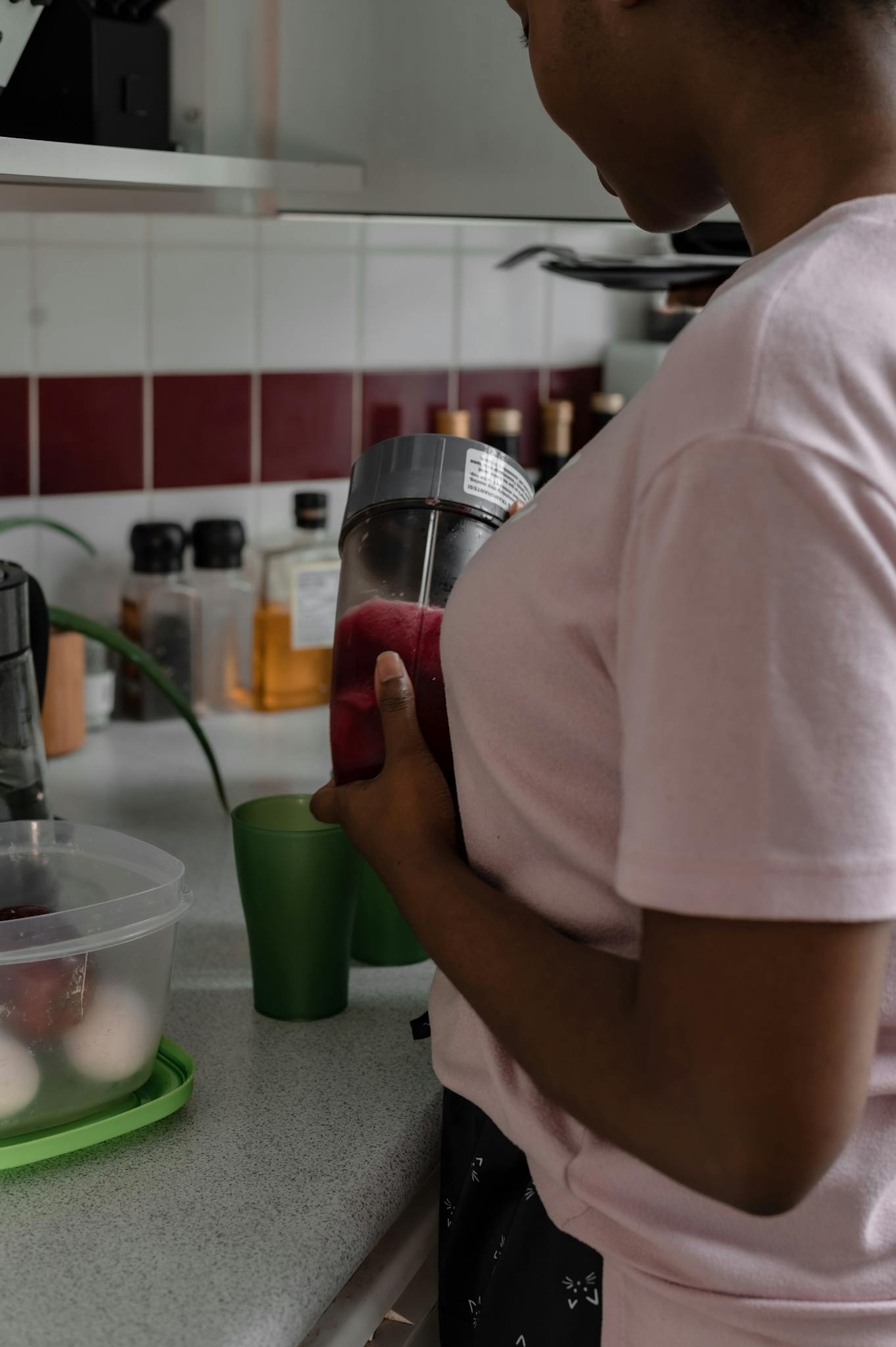 Close-up of a woman in a pink shirt making juice on a kitchen counter.