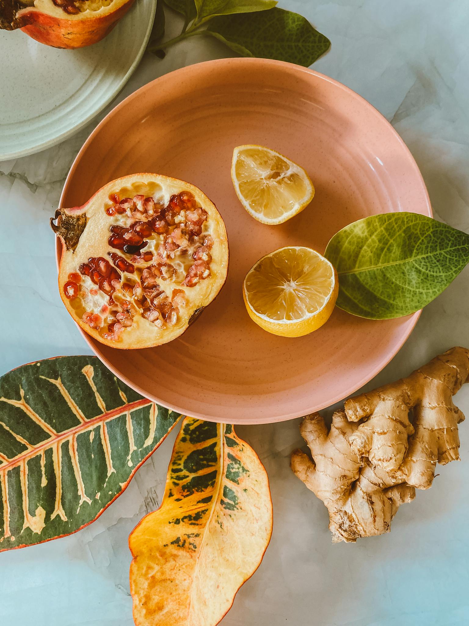 Colorful composition of sliced pomegranate, lemon, ginger and leaves on a plate.