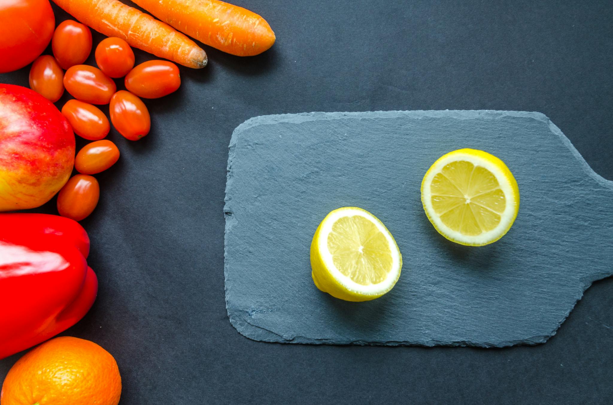 Top view of lemons, carrots, and fresh produce on a rustic slate board.