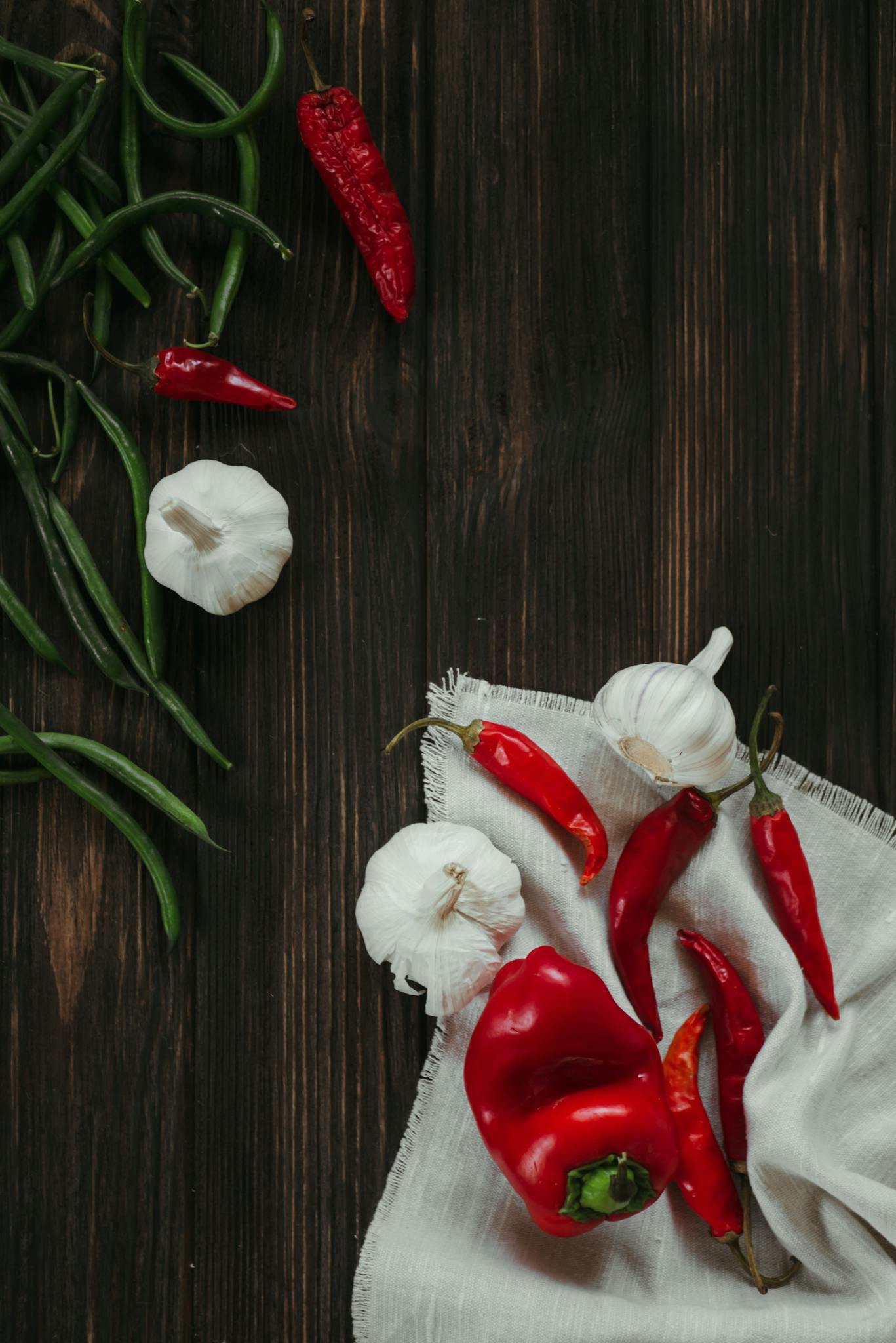 Vibrant red and green peppers with garlic on a rustic wooden table.